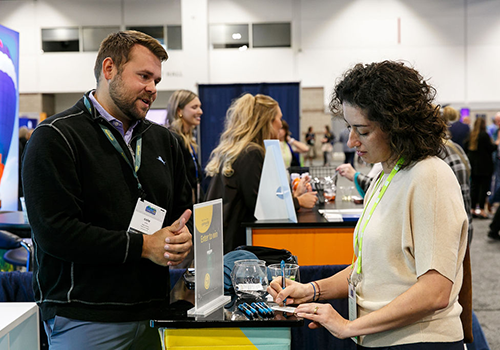 an woman writing notes while talking with exhibitor in conference hall