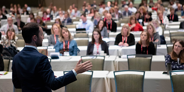 man in suit speaking to rows of conference attendees
